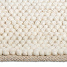 Macro close-up of the soft, pebble-like knotted texture of the cream Felix handmade rug.