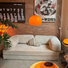 Goldenhour Adjustable Arc Floor Lamp with orange shade illuminating a cozy living room with retro art and beige sofa