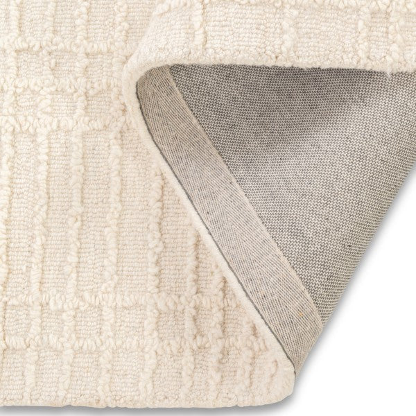 Folded corner of the neutral Hayes textured grid rug showing the underside woven backing construction