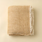 Folded woven blanket with frayed edges on a beige background