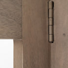 Macro detail of the antiqued metal hinge that connects the folding wooden frames of the Kade geometric shelving unit.