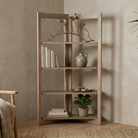 The Kade geometric shelving unit styled in a cozy living room corner with books and decor, next to a textured armchair.