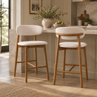 Two Linen Ash Wood Counter Stools with ivory linen seats and backs and natural wood frames beside a stone kitchen island.
