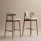 A pair of mid-century modern counter stools featuring a warm walnut-finished ash wood frame and a curved backrest upholstered in light textured linen.