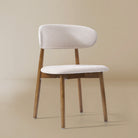 Angle view of the Linen Ash Wood Dining Side Chairs with curved upholstered backs and ash wood frames, shown in a neutral studio setting