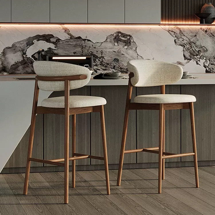 Two linen and walnut ash wood counter stools styled at a sleek modern kitchen island with marble countertops and dark wood cabinetry.
