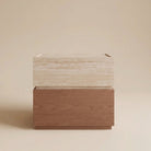 A modern two-tone wooden night stand with a travertine design top and a medium brown wood base, set against a solid beige studio background.