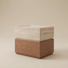 A modern two-tone side table featuring a warm brown wood-grain base and a light beige travertine stone top, set against a solid beige background.