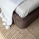 A close-up of the Lunelle bed corner with velvet upholstered bed frame, cream bedding, a white throw blanket with pom-poms, and a textured beige rug.