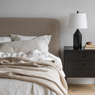 Bedroom with a Lunelle bed featuring beige bedding and pillows, a nightstand with a lamp and books.