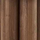 Detailed close-up of the Lyric table base highlighting the rich walnut wood grain and vertical clustered cylinder design.