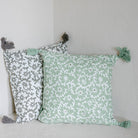 Two patterned pillows with tassels on a light gray surface against a white wall.