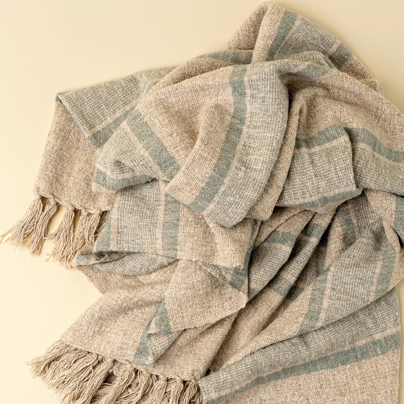 Textured blanket with blue and beige stripes and tassels on a beige background
