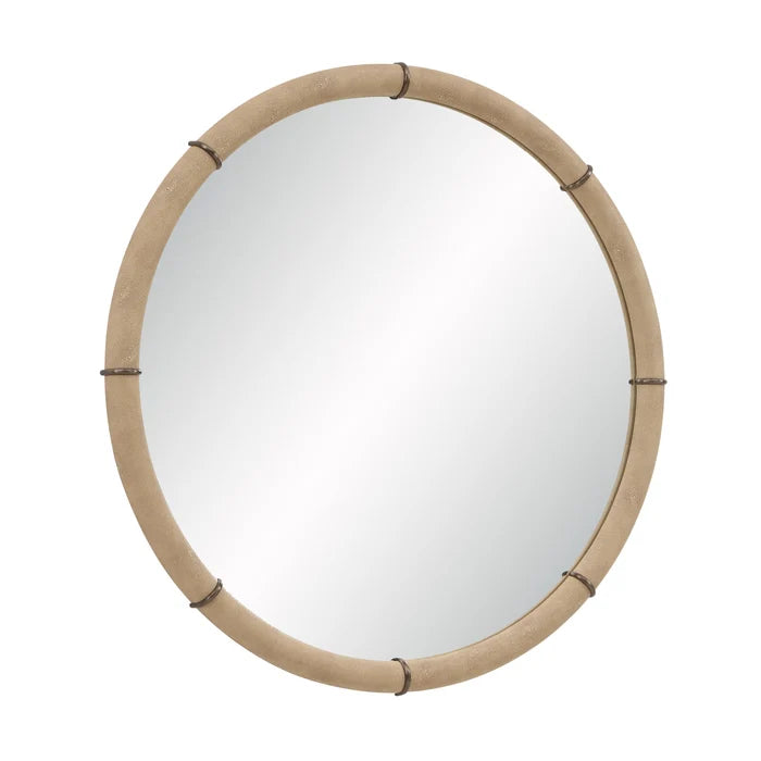 Angled view of the Mirelle Round Wall Mirror showing its circular form and beige vegan leather frame with antique metal band accents.