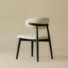 Back angled view of the Modern Leather Ash Wood Dining Chair revealing the solid black wood support bar cradling the cream upholstered backrest.