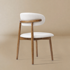 Rear three-quarter view of a cream PU leather dining chair with a curved walnut-finished ash wood frame featuring the Modern PU Leather Ash Wood Dining Side...