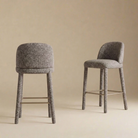 A pair of Myla upholstered counter stools showcasing their curved backrests and seamless light grey textured fabric.