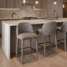 Two light grey textured Myla counter stools styled at a white marble kitchen island next to a home bar setup.