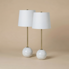A set of two Nox table lamps featuring spherical white marble bases, slender brass stems, and white linen shades.
