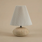 Table lamp with pleated white shade and travertine base on beige background