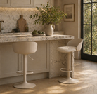 Modern kitchen with marble island and bar stools, featuring a vase with greenery.