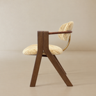 [Orsino Dining Chair] Side profile showing the angled wood frame, upholstered seat and backrest, wrapped armrest, and curved brass-toned back support.