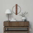 Orvella walnut and antique brushed brass wall clock displayed above a wood console with a table lamp and decorative vase.