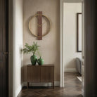 Orvella walnut and antique brushed brass wall clock mounted above a wood cabinet in a softly lit hallway.
