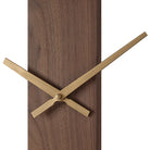 Close-up of the Orvella wall clock showing the antique brushed brass hands against the walnut wood panel.