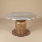 Ottilie round dining table with marble top and wooden base on beige studio background.