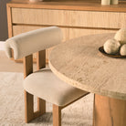 Styled detail of the Romina travertine dining table with an upholstered oak dining chair