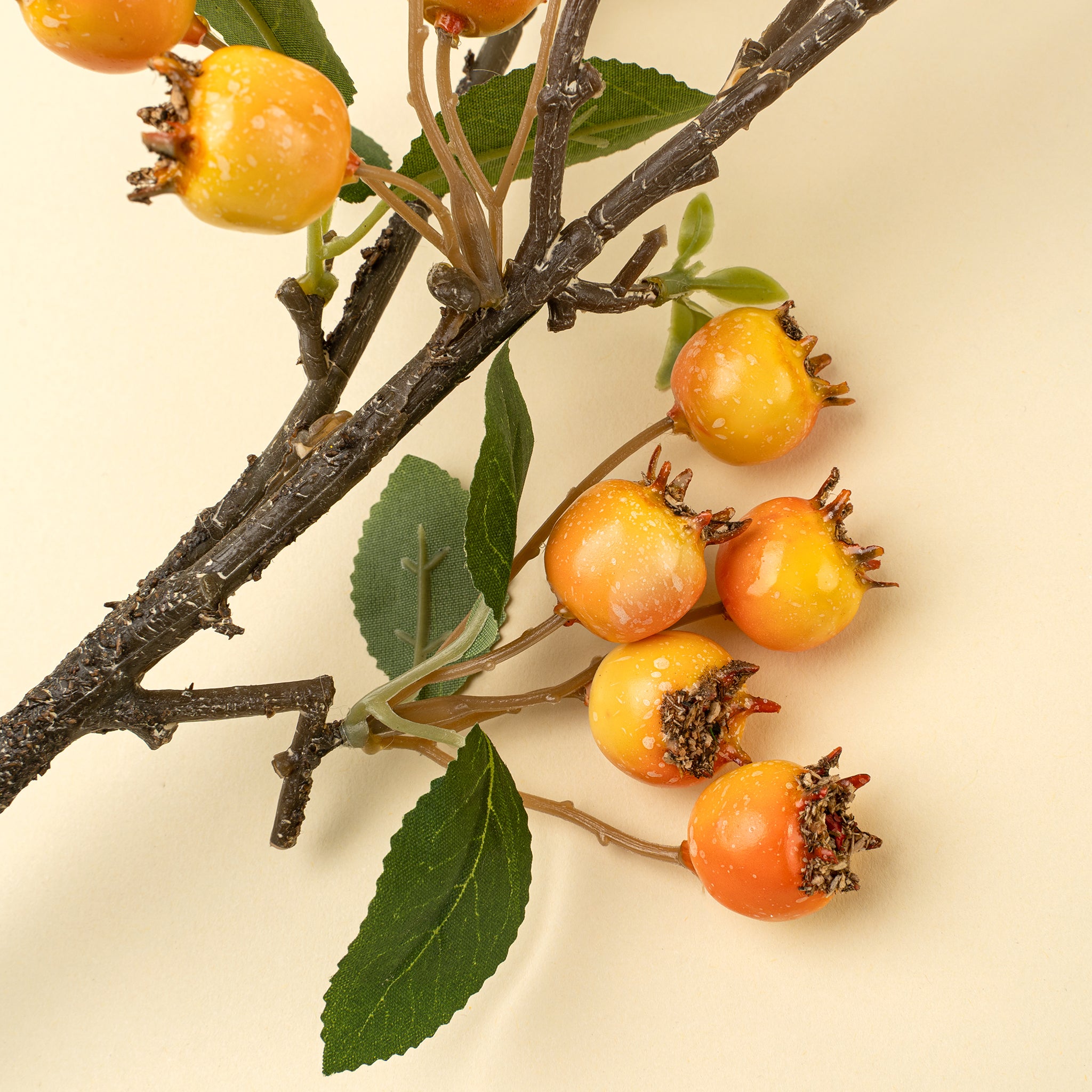 Artificial branch with orange berries and green leaves on a beige background