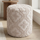 Textured beige ottoman on a wooden floor with a wooden table in the background