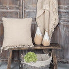 Decorative setting with a textured pillow, vases, and a basket on a wooden table against a rustic wooden wall.