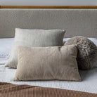 Close-up lifestyle view of the Serenity cushion set on white bedding, highlighting the blend of soft grey and tan natural tones.