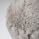 Close-up detail of the round Serenity accent pillow highlighting the soft, shaggy faux fur texture in a warm taupe.