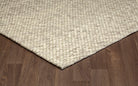 Corner view of the cream Silas hand-woven wool rug resting on a wooden floor, showcasing its textured edge