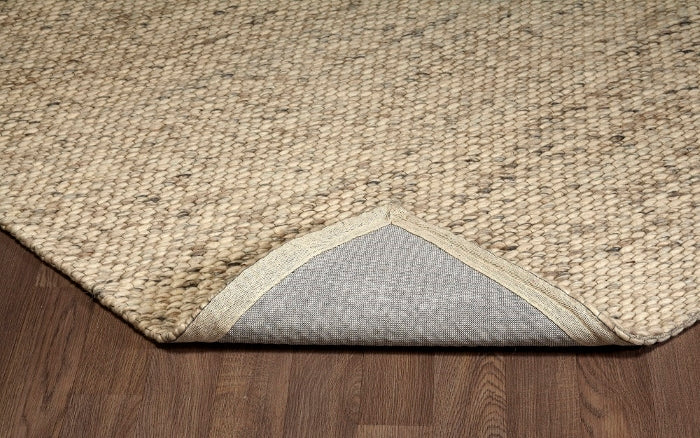Folded corner of the beige Silas wool rug, revealing its chunky looped surface and sturdy backing