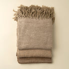 Folded beige blanket with frayed edges on a beige background