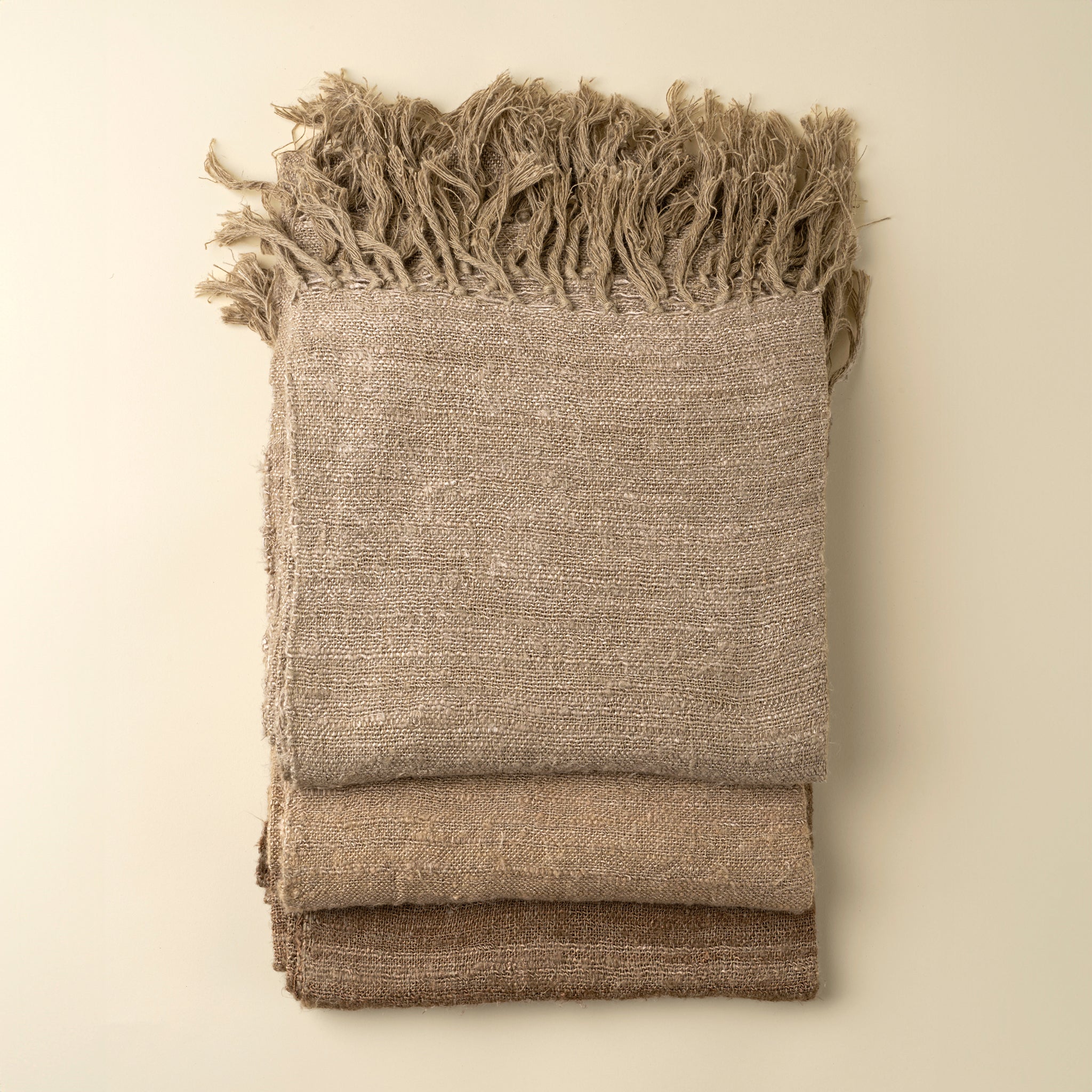 Folded beige blanket with frayed edges on a beige background