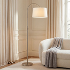 Solenne Arc Floor Lamp in polished nickel styled beside a curved cream sofa in a bright living room.