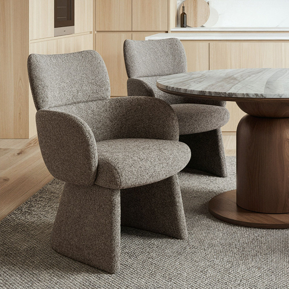 Two charcoal upholstered chairs and a round wooden table in a room with wooden flooring and cabinets featuring the Soren Bouclé Dining Chair