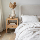 The Sutton oak nightstand styled next to a cream bouclé upholstered bed with linen bedding and natural pampas grass.