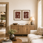 Two framed floral prints on a wall above a wooden dresser with baskets and fruit.