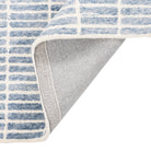 Tessera Hand-Tufted Wool Grid Rug in blue folded back to show its cotton backing and finished edge.