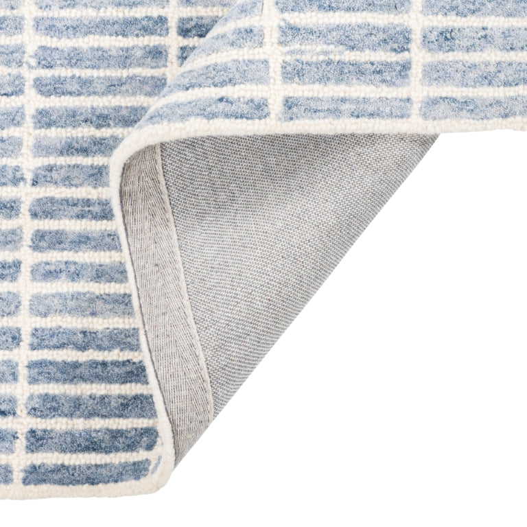 Tessera Hand-Tufted Wool Grid Rug in blue folded back to show its cotton backing and finished edge.