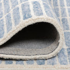 Folded Tessera Hand-Tufted Wool Grid Rug in blue showing the wool pile, bound edge, and cotton backing.