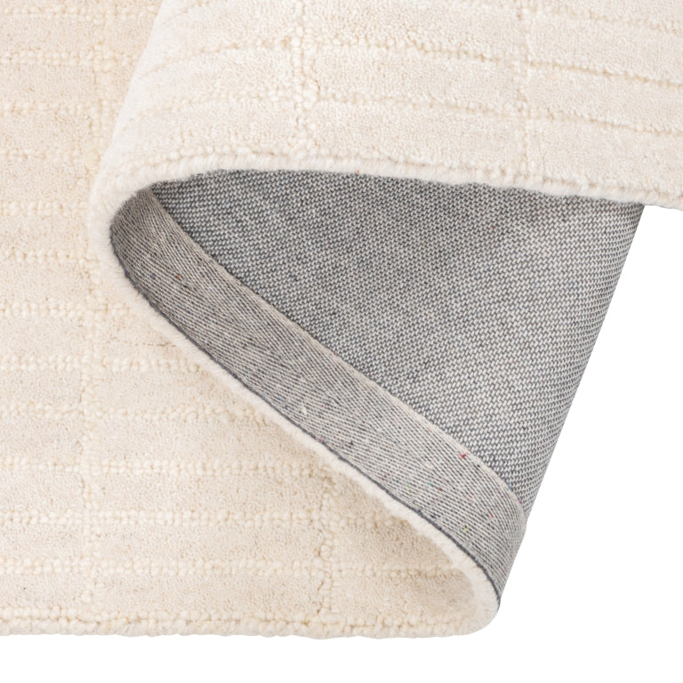 Tessera Hand-Tufted Wool Grid Rug in ivory folded back to show its cotton backing and finished edge.