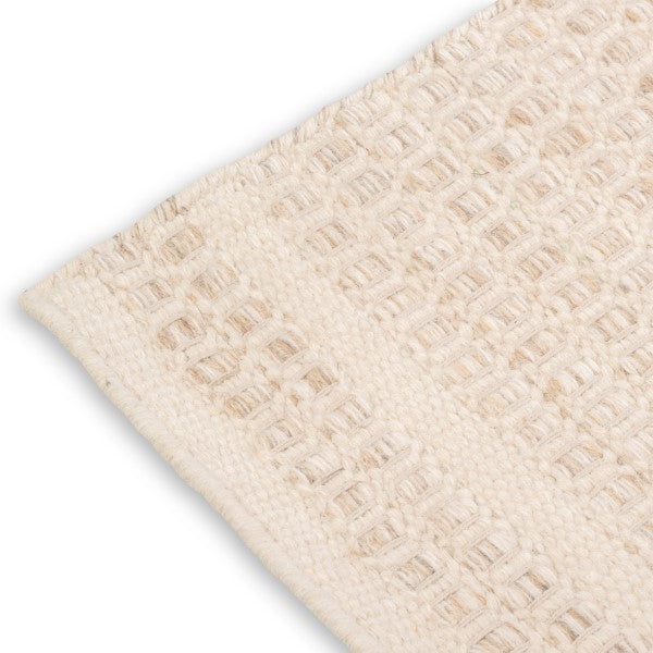 Close-up corner detail of the ivory Theo wool rug showing the neat edge binding and chunky woven texture