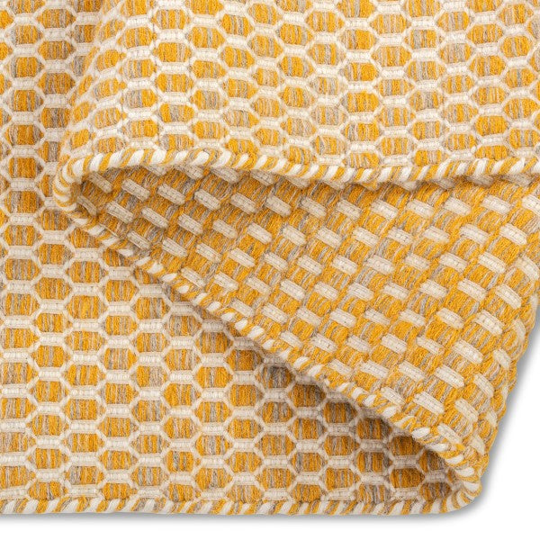 A folded corner of the yellow Theo hand-woven wool rug, showing its thickness, durable backing, and soft texture